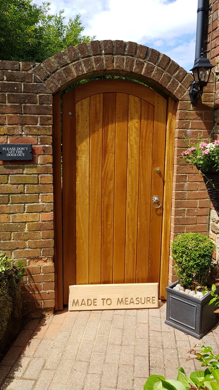 Arched timber gate beneath a brick arch with a Made To Measure board at its base